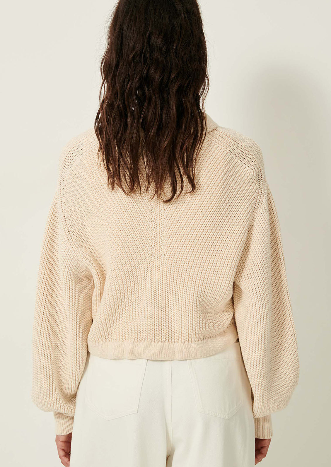 A woman wearing a cream knit sweater with collar, button front and tie waist.