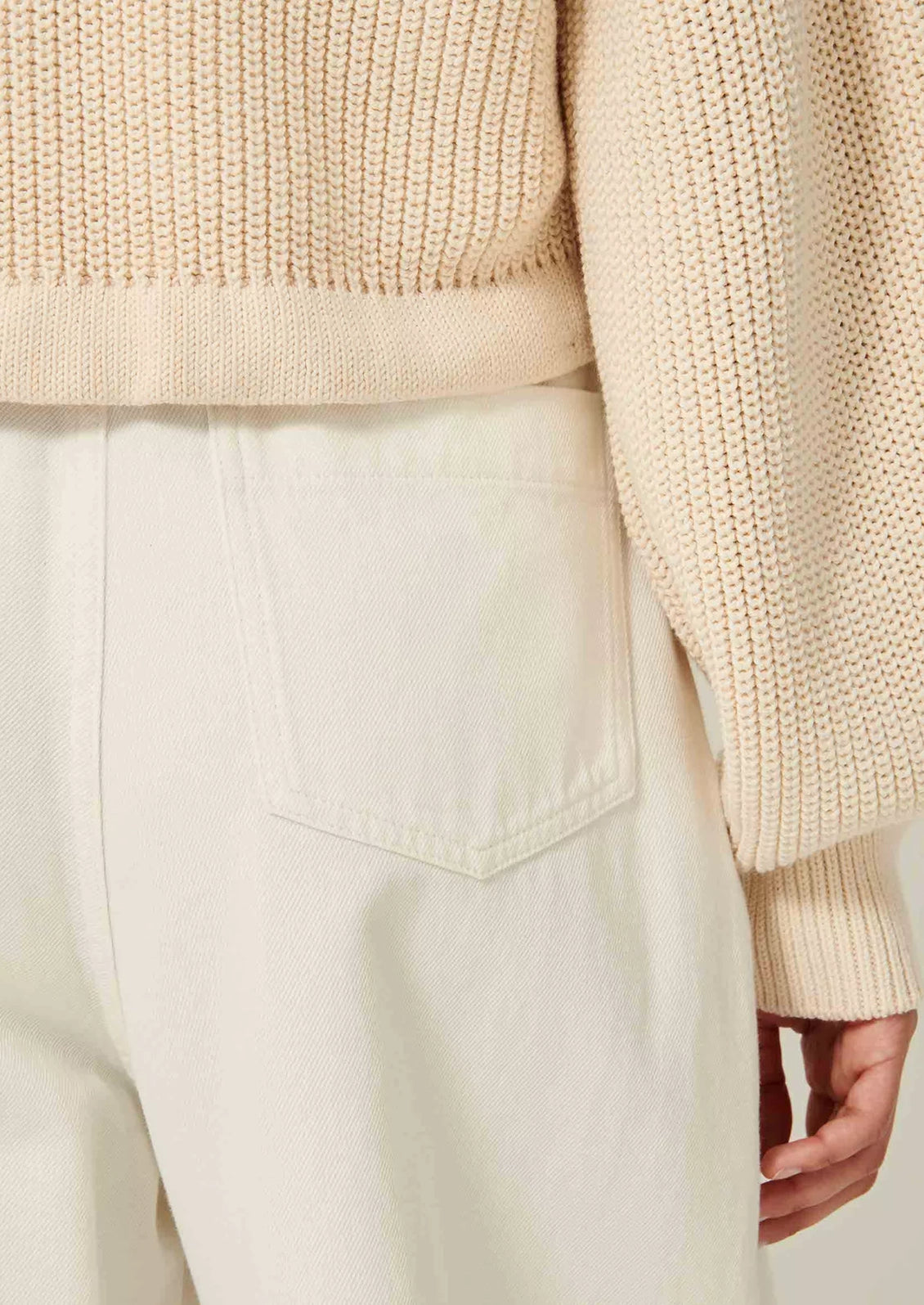 A woman wearing a cream knit sweater with collar, button front and tie waist.