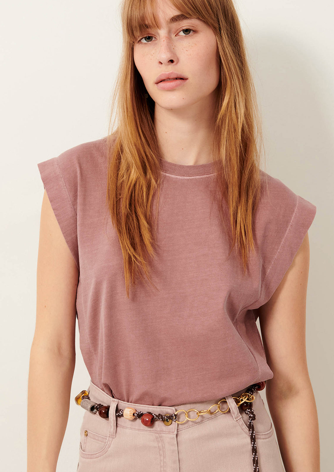 A person wearing a muscle tee in muted mauve color.