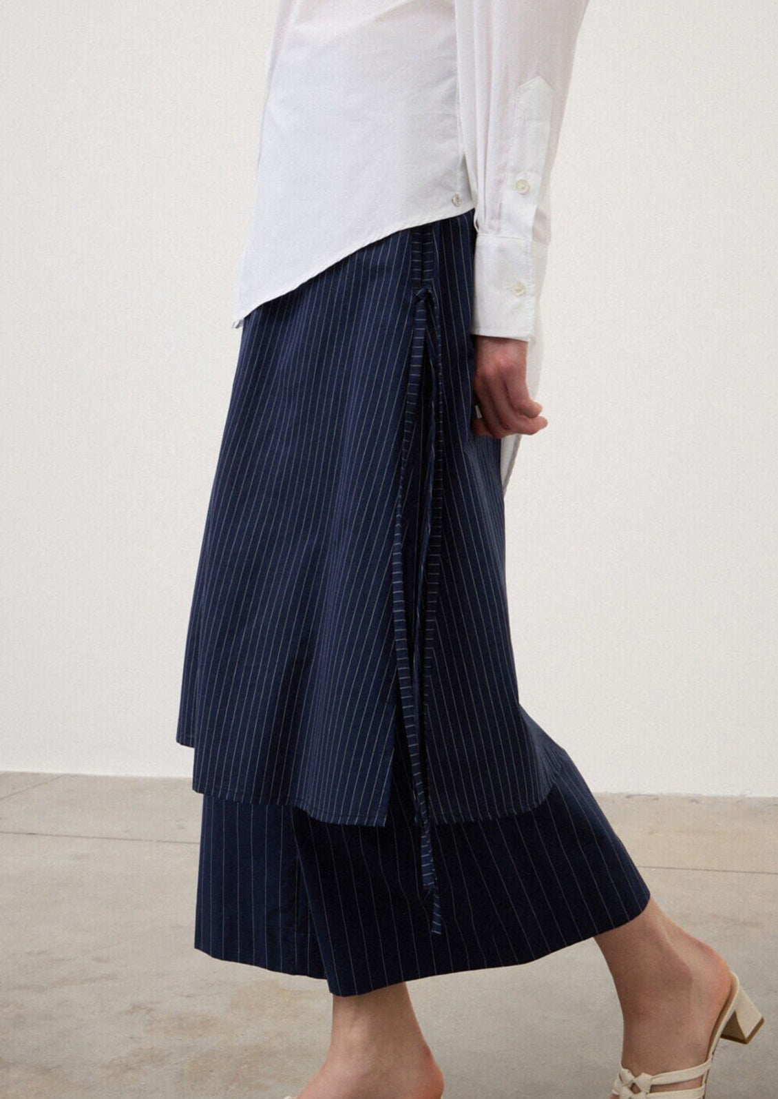A person wearing a pair of navy blue pinstripe pants with skirt-like layer over top.