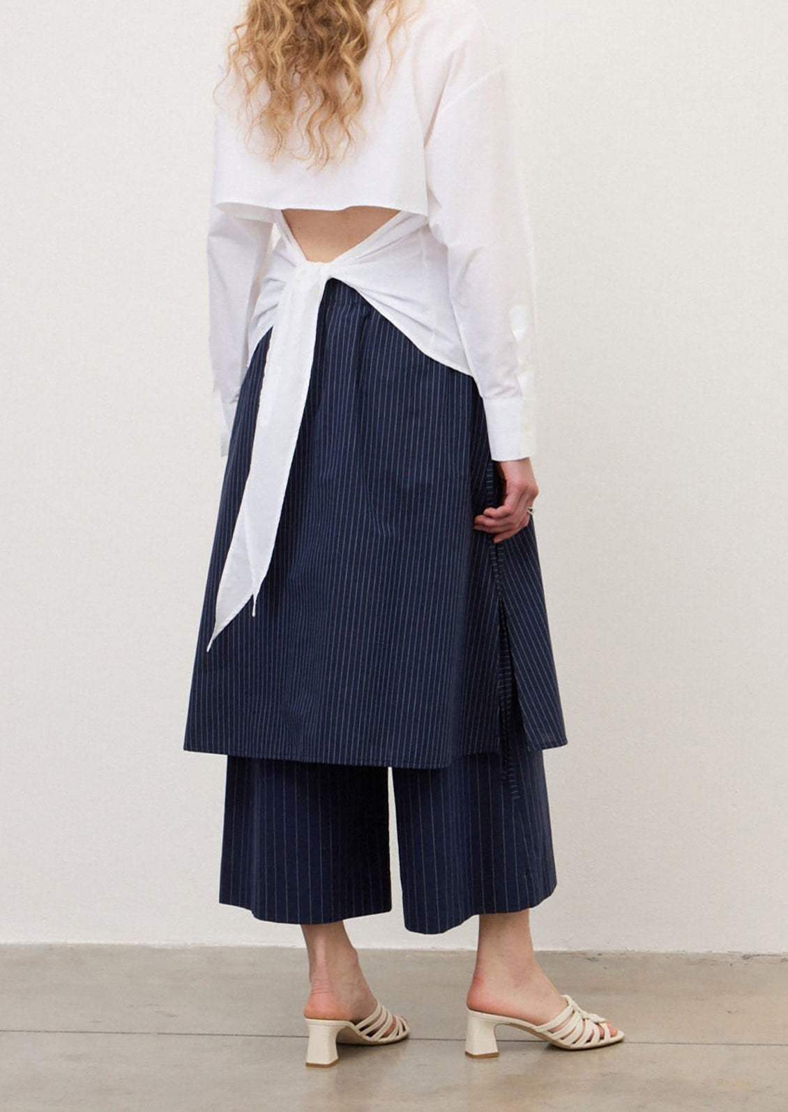 A person wearing a pair of navy blue pinstripe pants with skirt-like layer over top.