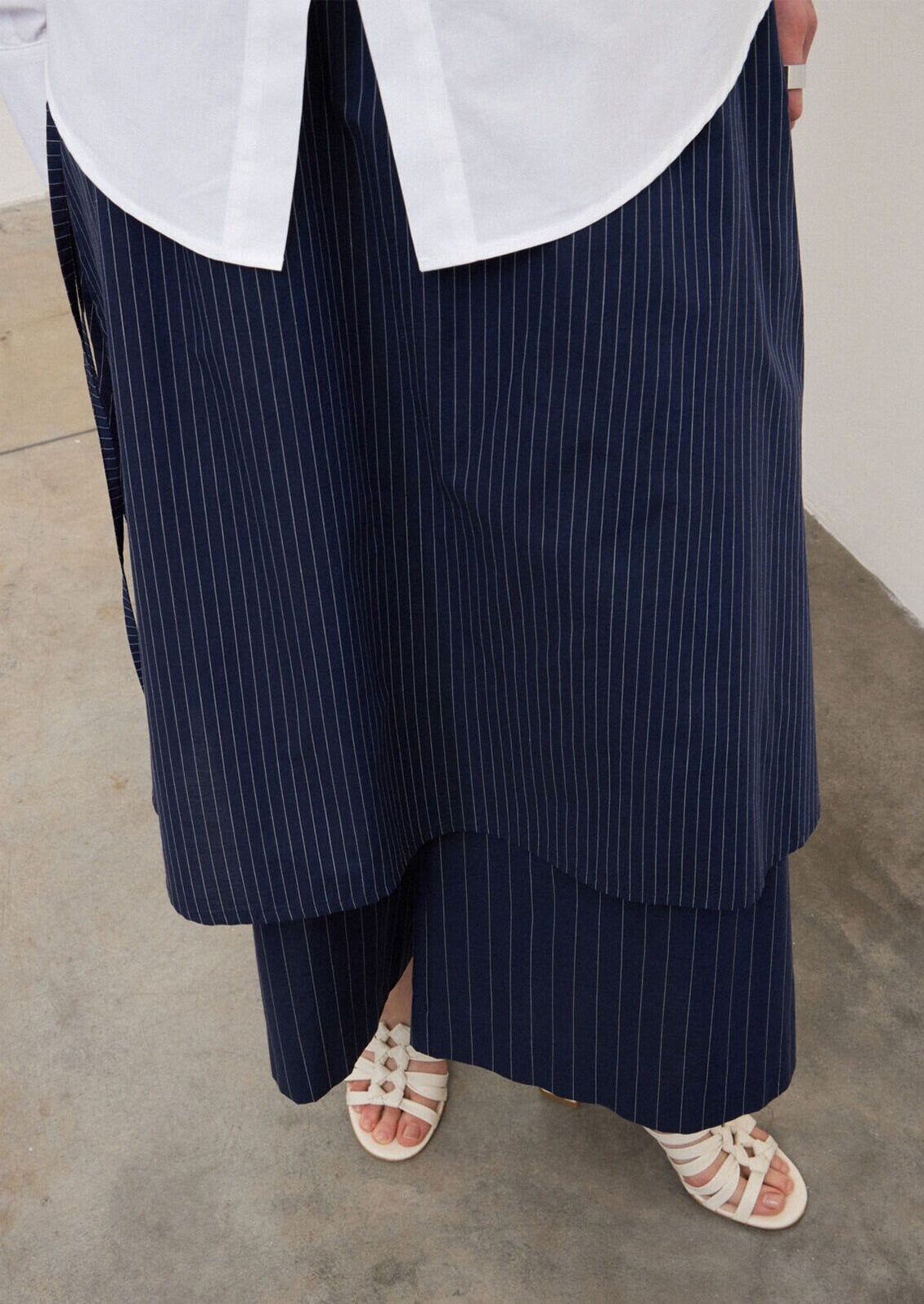 A person wearing a pair of navy blue pinstripe pants with skirt-like layer over top.