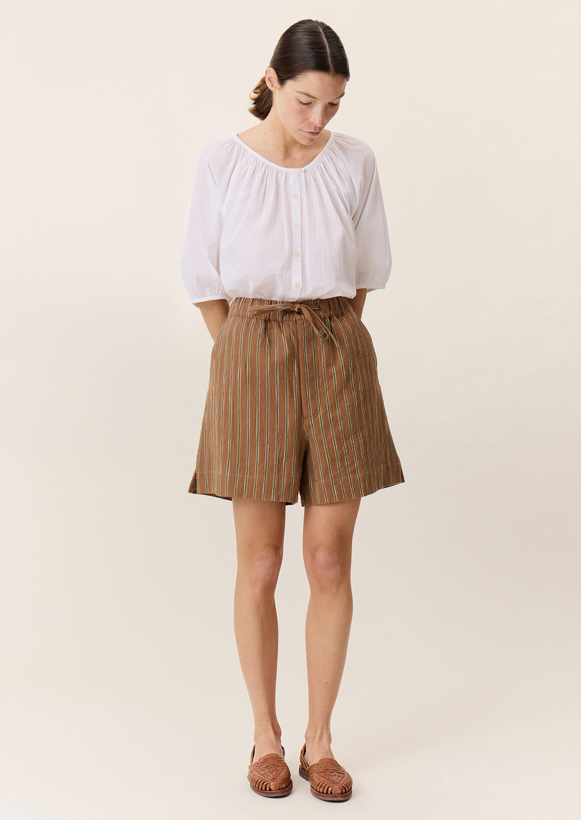 A person wearing a pair of tailored shorts in brown with green stripe pattern.