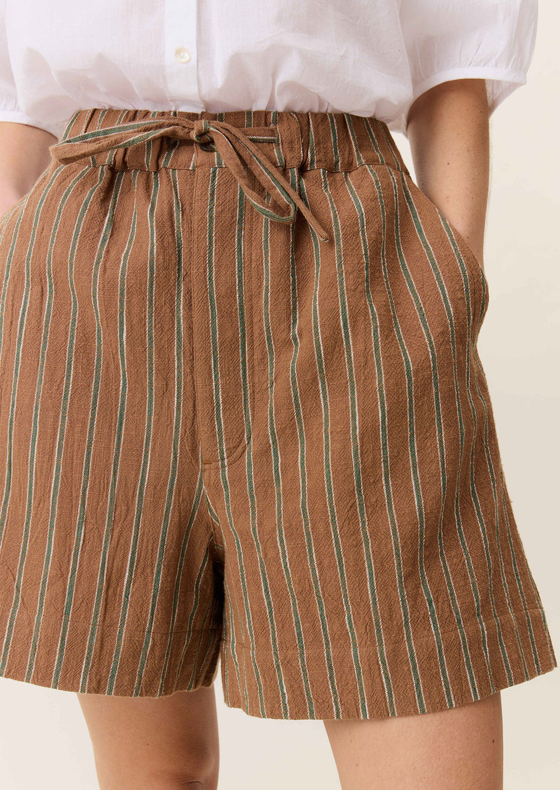 A person wearing a pair of tailored shorts in brown with green stripe pattern.