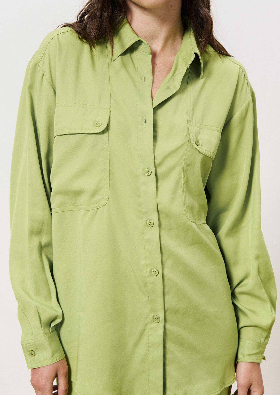 A woman wearing a button front shirt in green with double button flap pocket detail at chest.