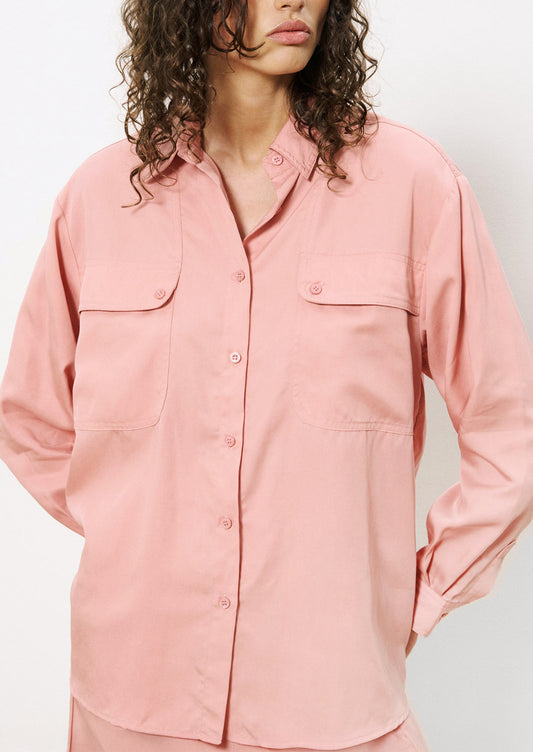 A woman wearing a button front shirt in pink with double button flap pocket detail at chest.