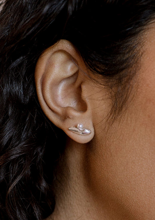 A woman wearing a pair of silver sliver shaped earrings with resting pearl.