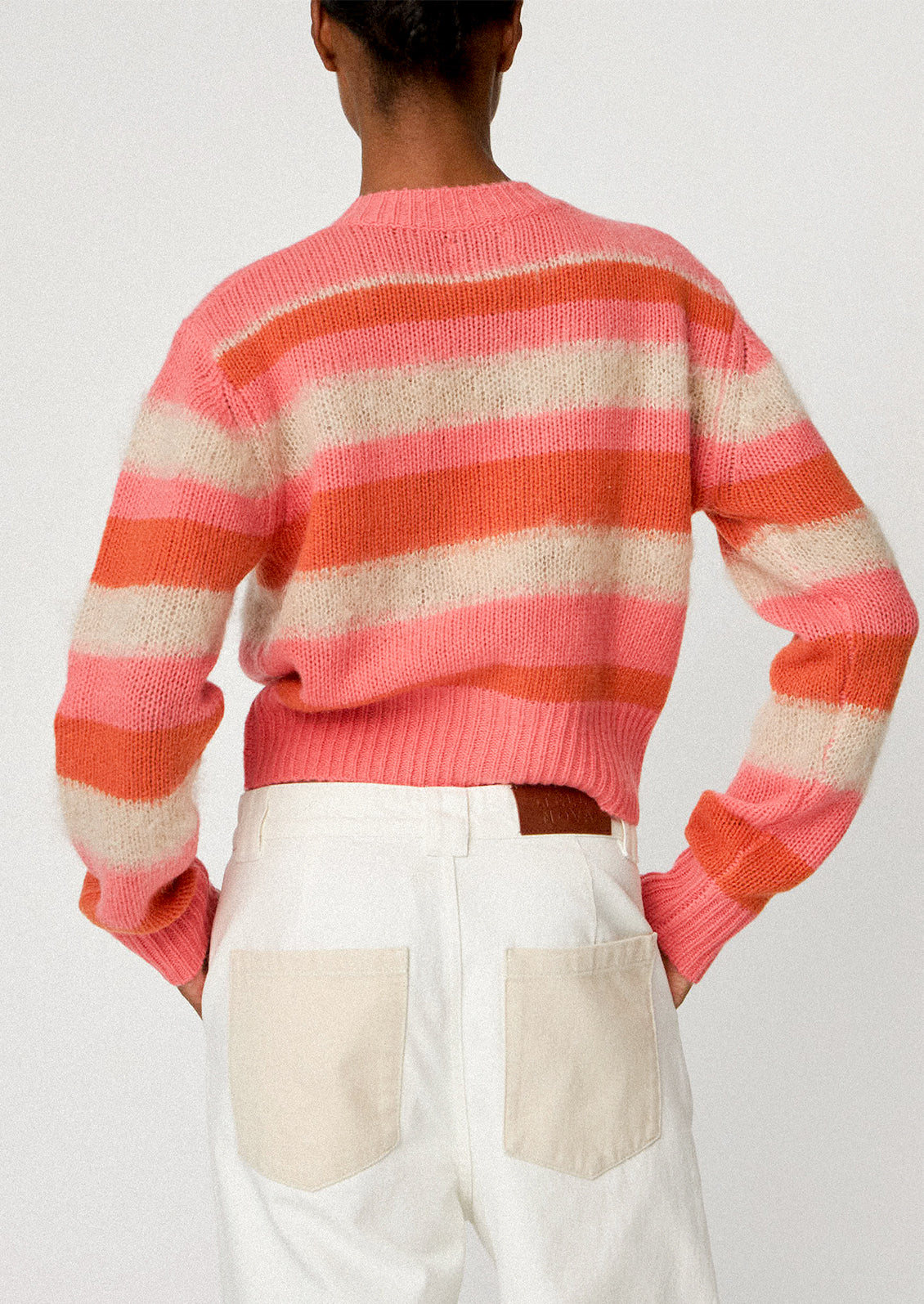 A woman wearing a button front cardigan sweater in pink, orange and ivory stripes.