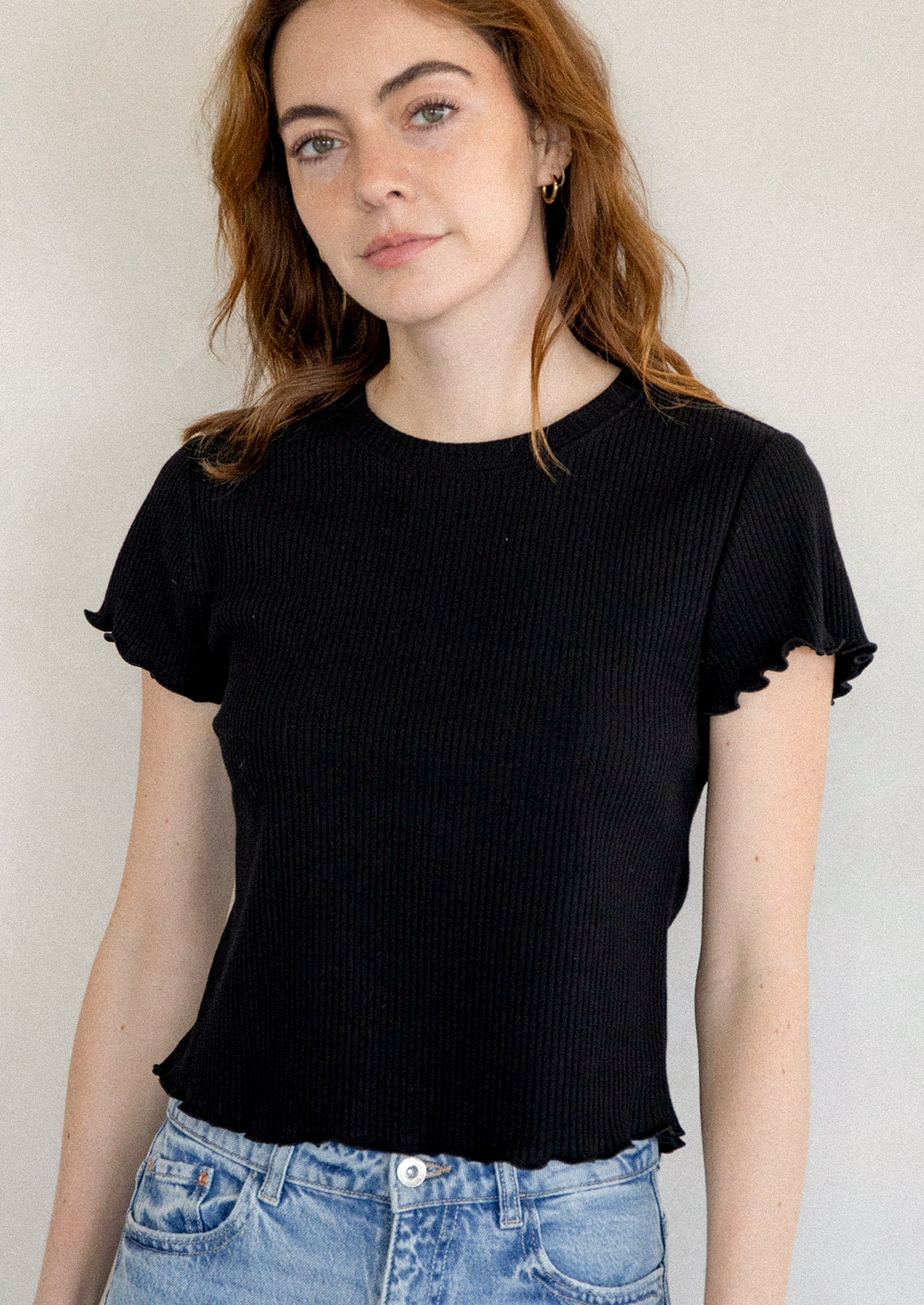 A woman wearing a black short sleeve baby tee with ruffled sleeve and hem.