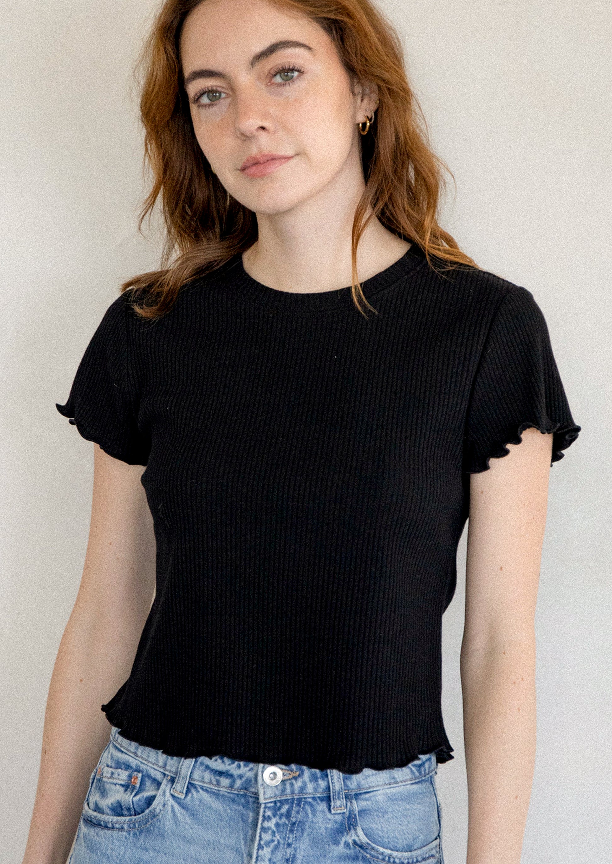A woman wearing a black short sleeve baby tee with ruffled sleeve and hem.