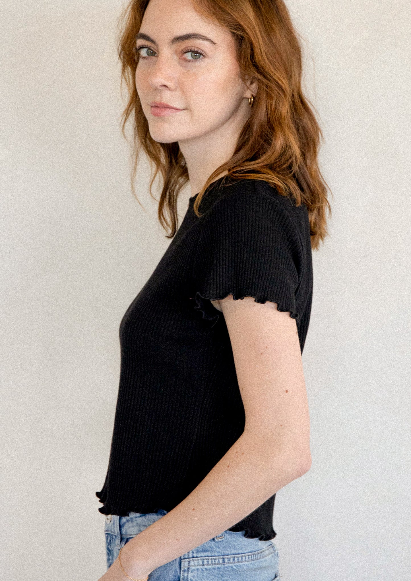 A woman wearing a black short sleeve baby tee with ruffled sleeve and hem.