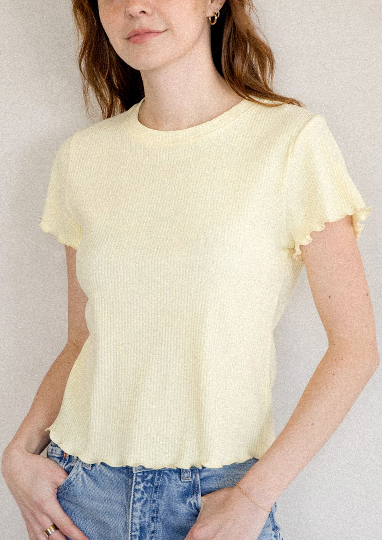 A woman wearing a yellow short sleeve baby tee with ruffled sleeve and hem.