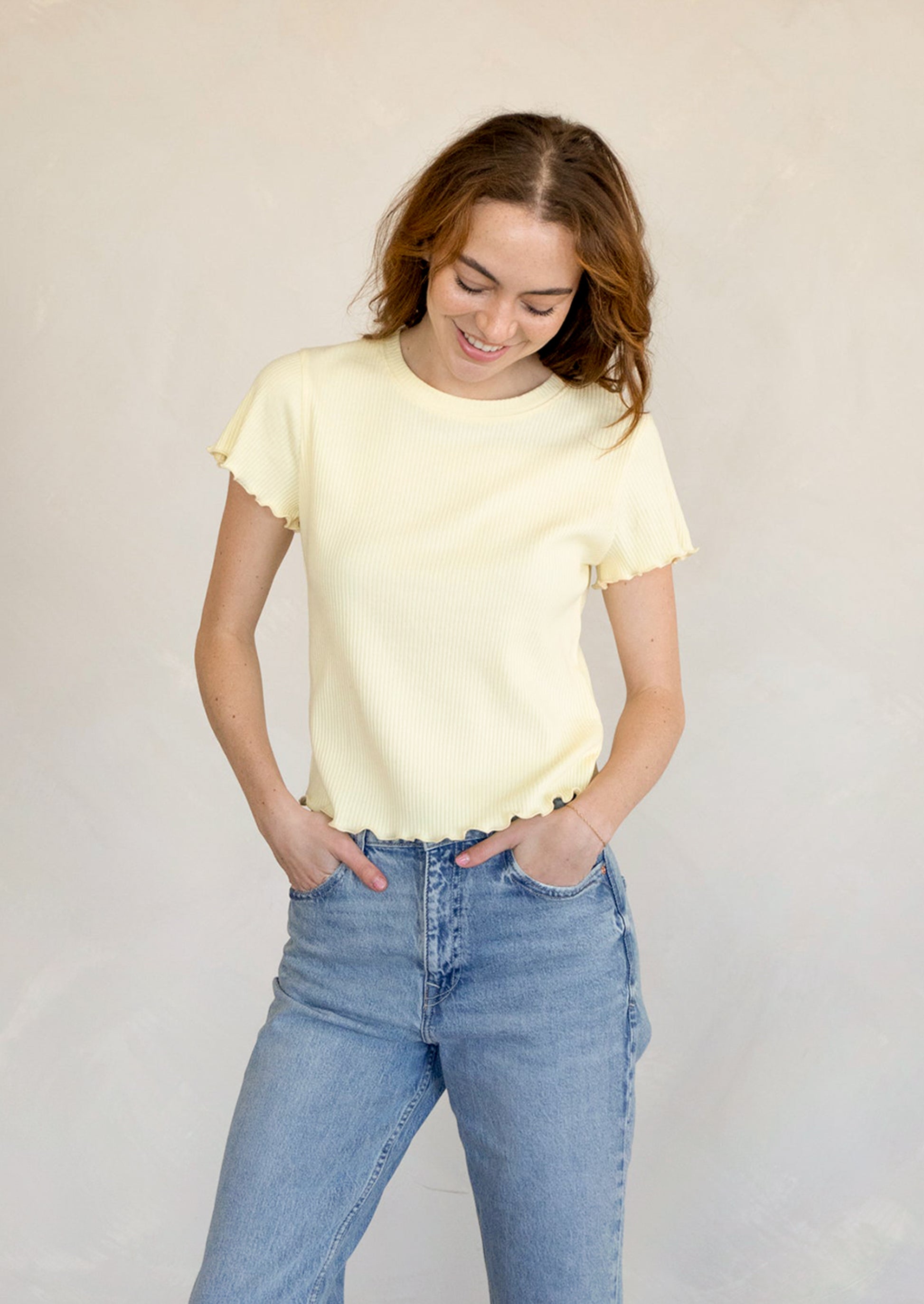 A woman wearing a butter yellow short sleeve baby tee with blue jeans.