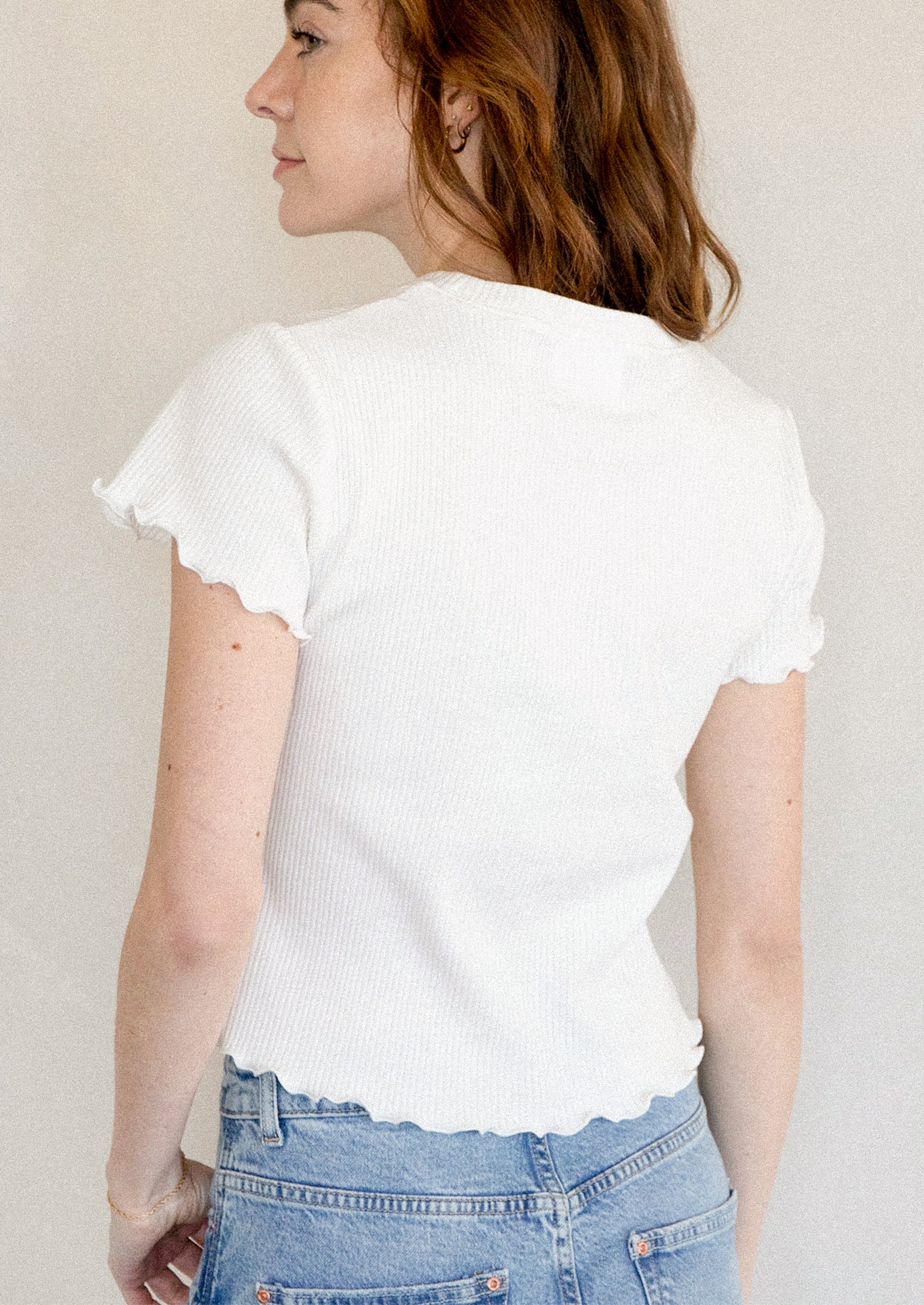A woman wearing a white short sleeve baby tee with ruffled sleeve and hem.