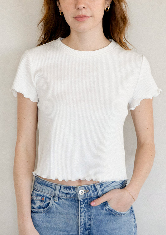 A woman wearing a white short sleeve baby tee with ruffled sleeve and hem.