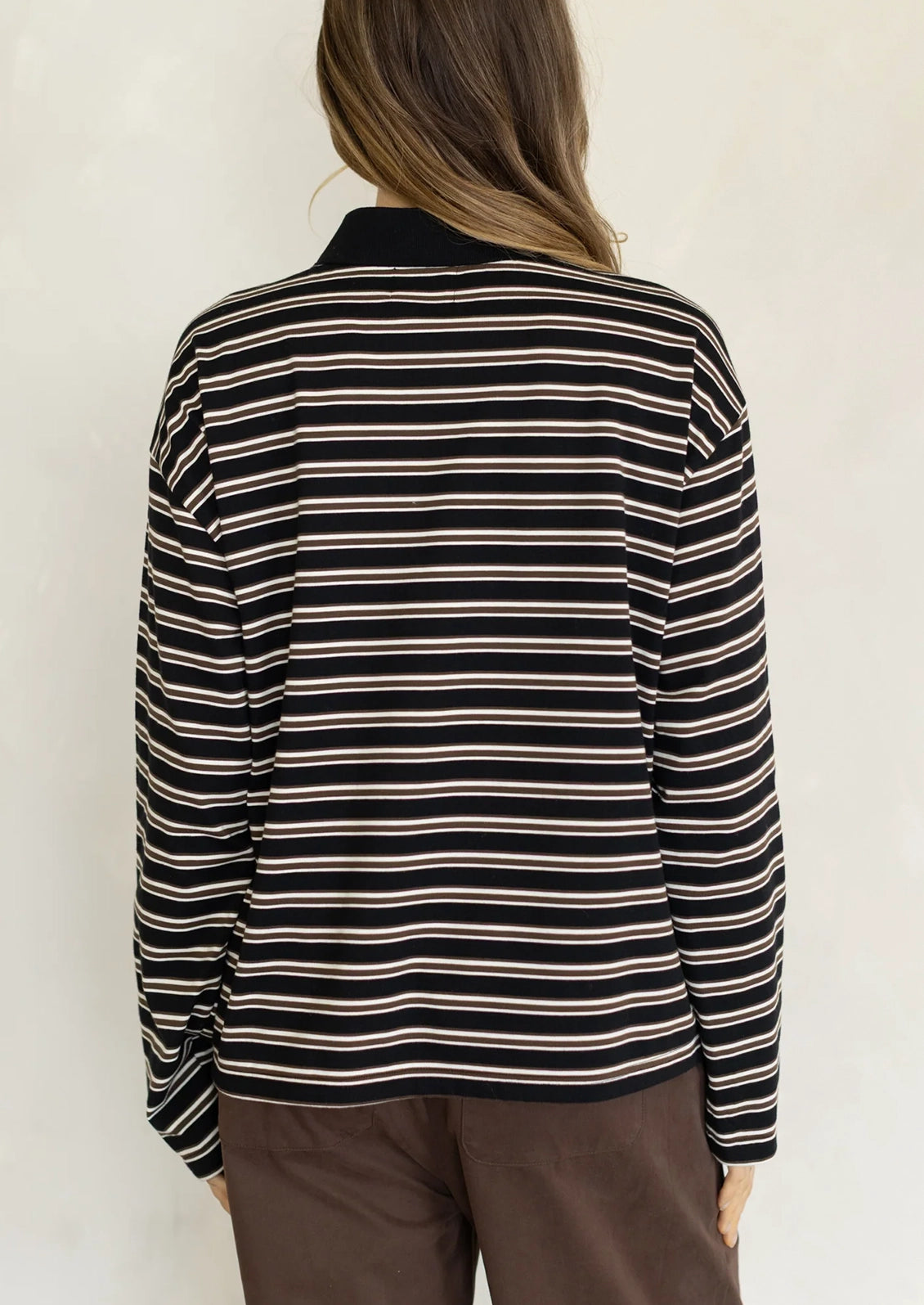 A woman wearing a long sleeve striped t-shirt with polo collar, black with white and brown stripes.