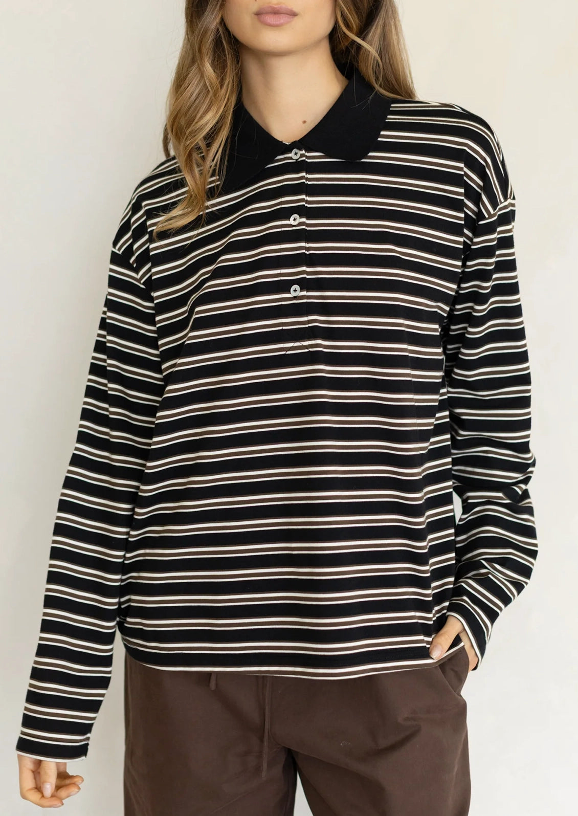 A woman wearing a long sleeve striped t-shirt with polo collar, black with white and brown stripes.