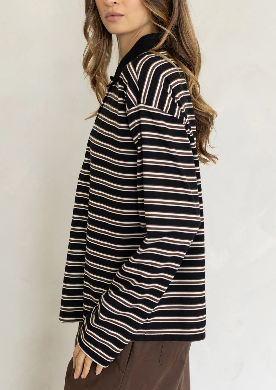 A woman wearing a long sleeve striped t-shirt with polo collar, black with white and brown stripes.