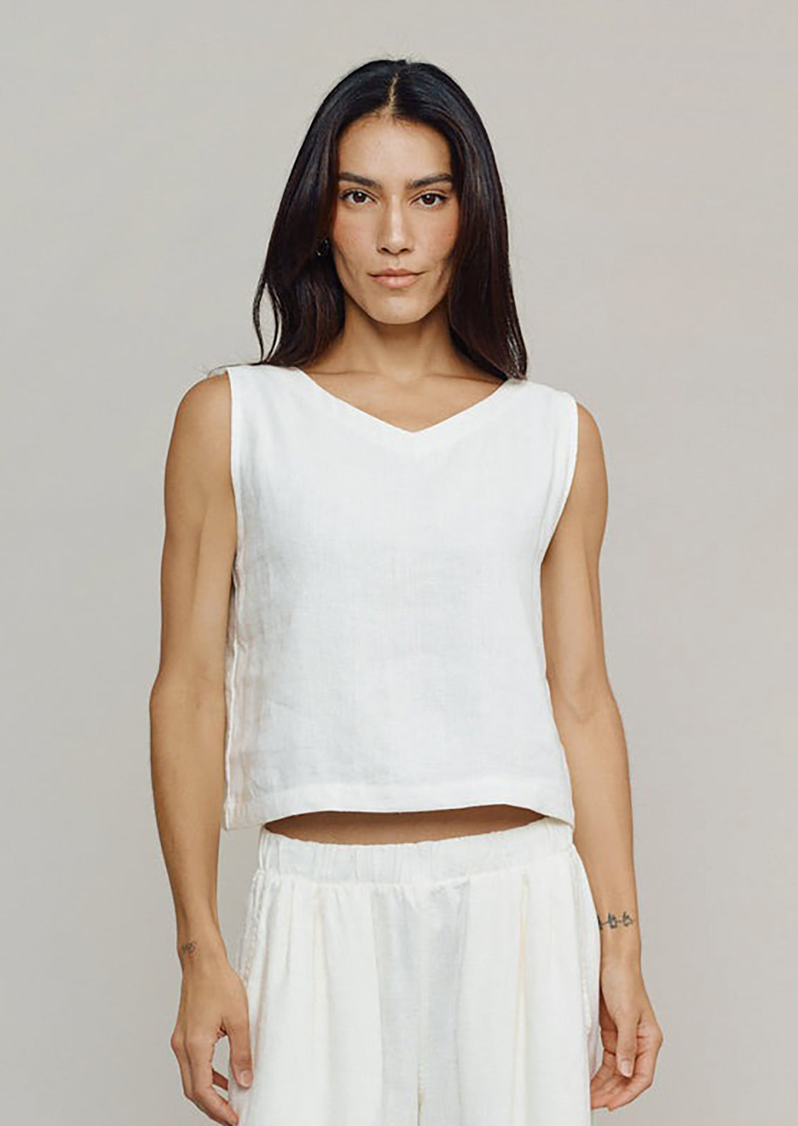Woman wearing a white sleeveless top and skirt on a plain background