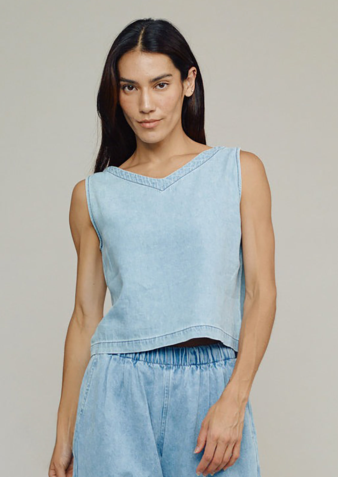 Woman wearing a light blue sleeveless top and pants against a neutral background