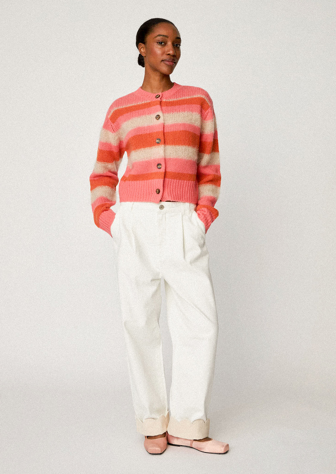 A woman wearing a button front cardigan sweater in pink, orange and ivory stripes.