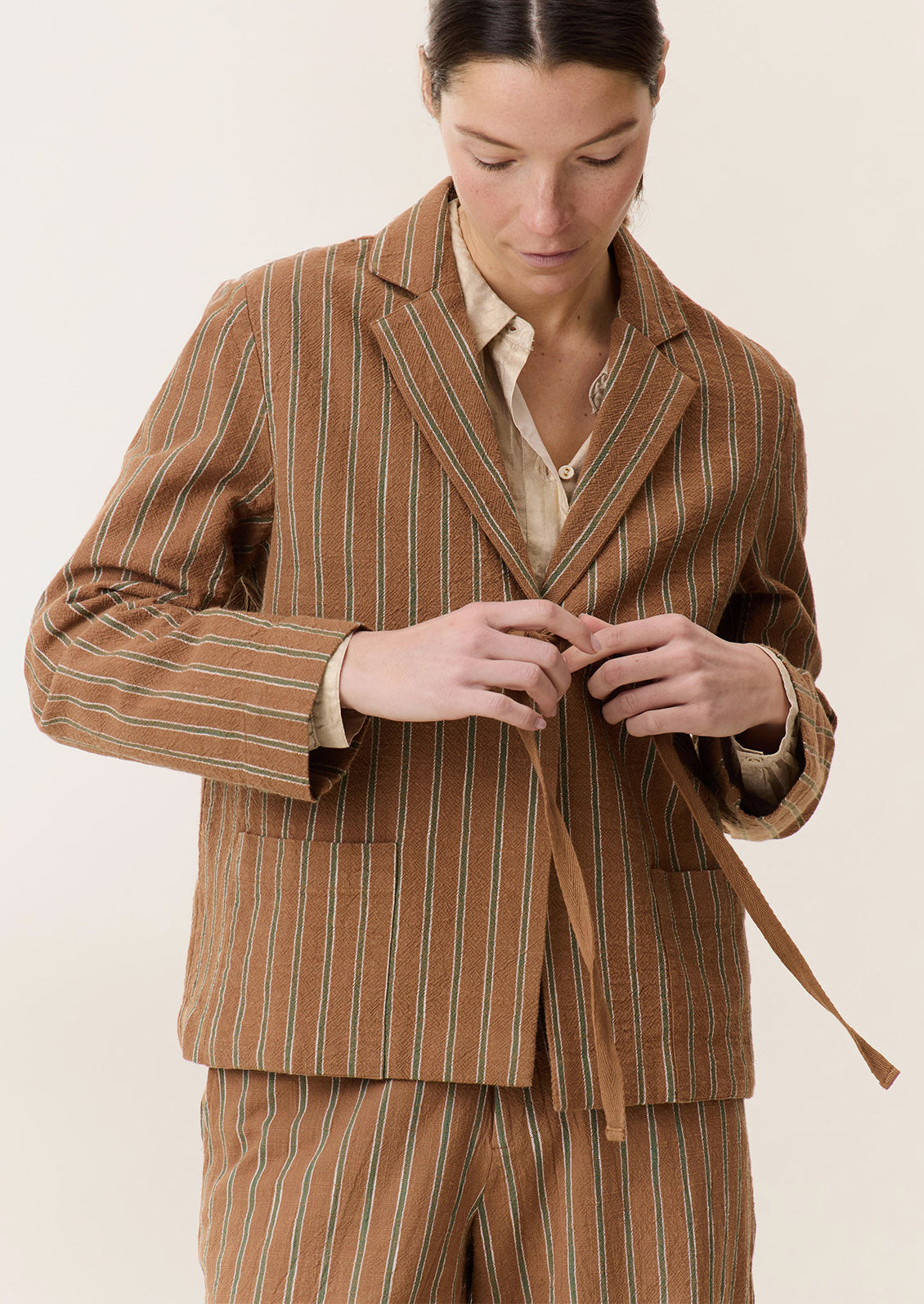 A woman wearing a brown suit jacket with green stripe pattern and tie front closure.