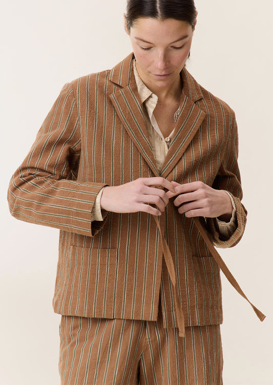 A woman wearing a brown suit jacket with green stripe pattern and tie front closure.