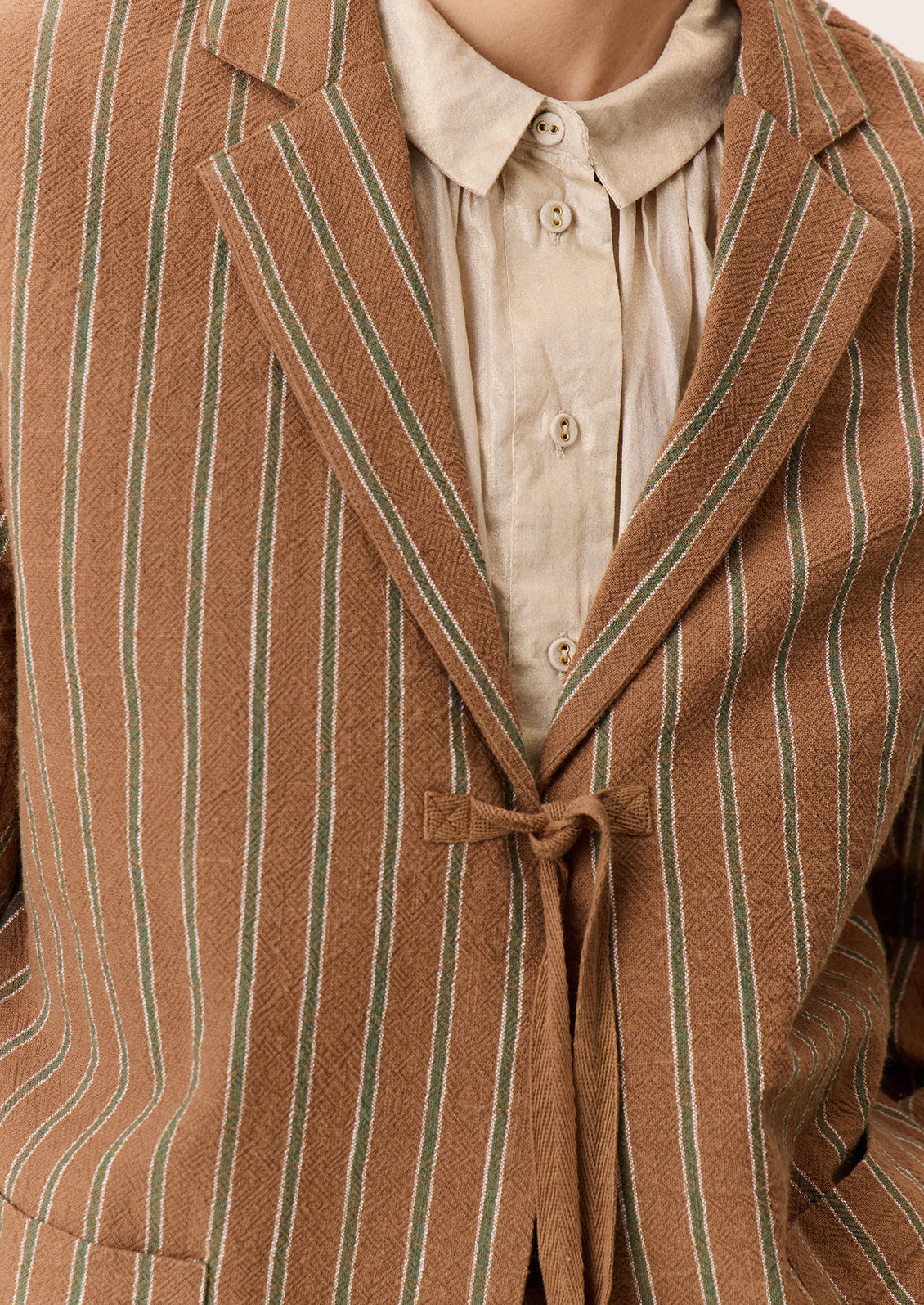 A woman wearing a brown suit jacket with green stripe pattern and tie front closure.