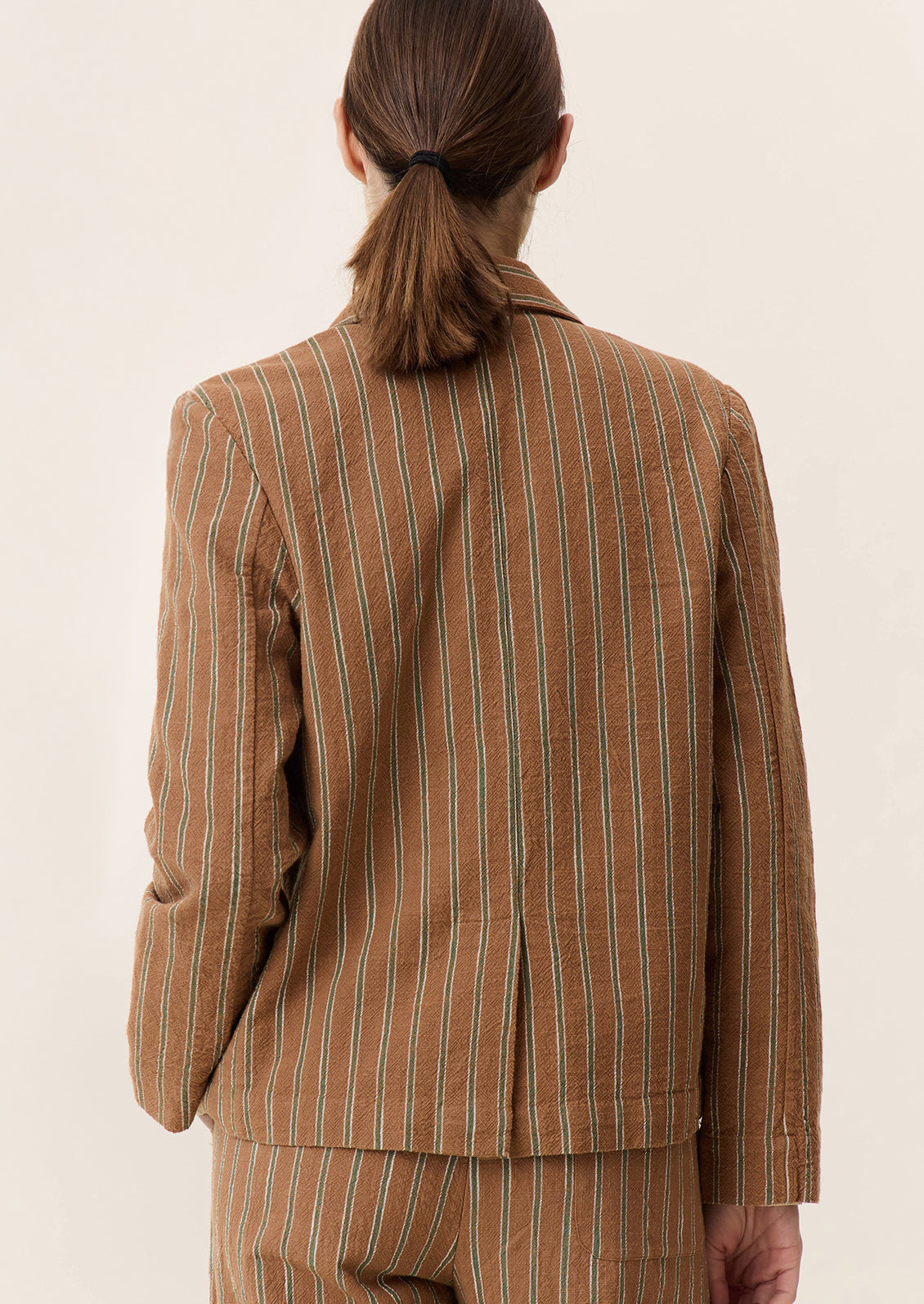 A woman wearing a brown suit jacket with green stripe pattern and tie front closure.