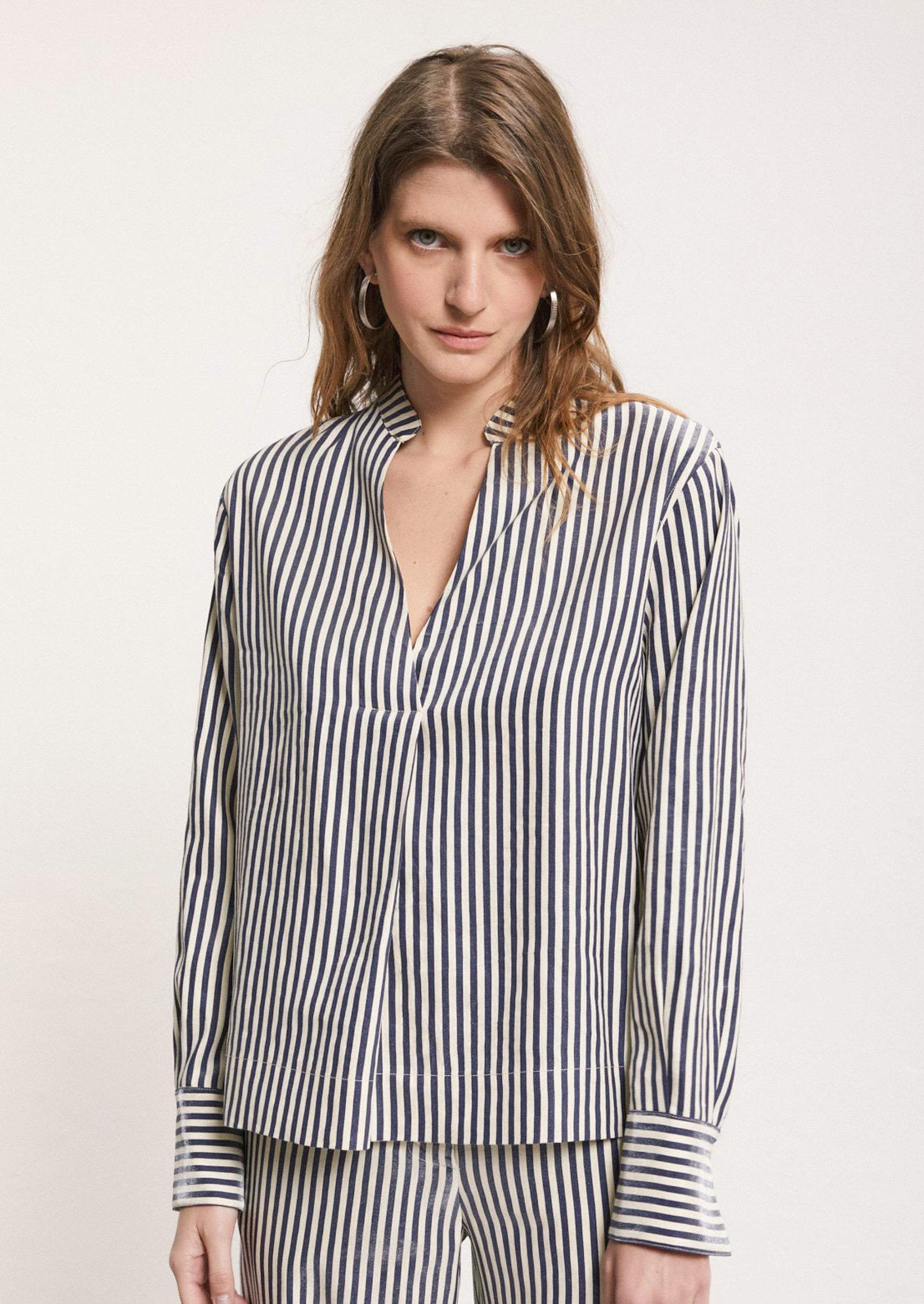 A woman wearing a striped long sleeve shirt in metallic navy blue and cream stripe.