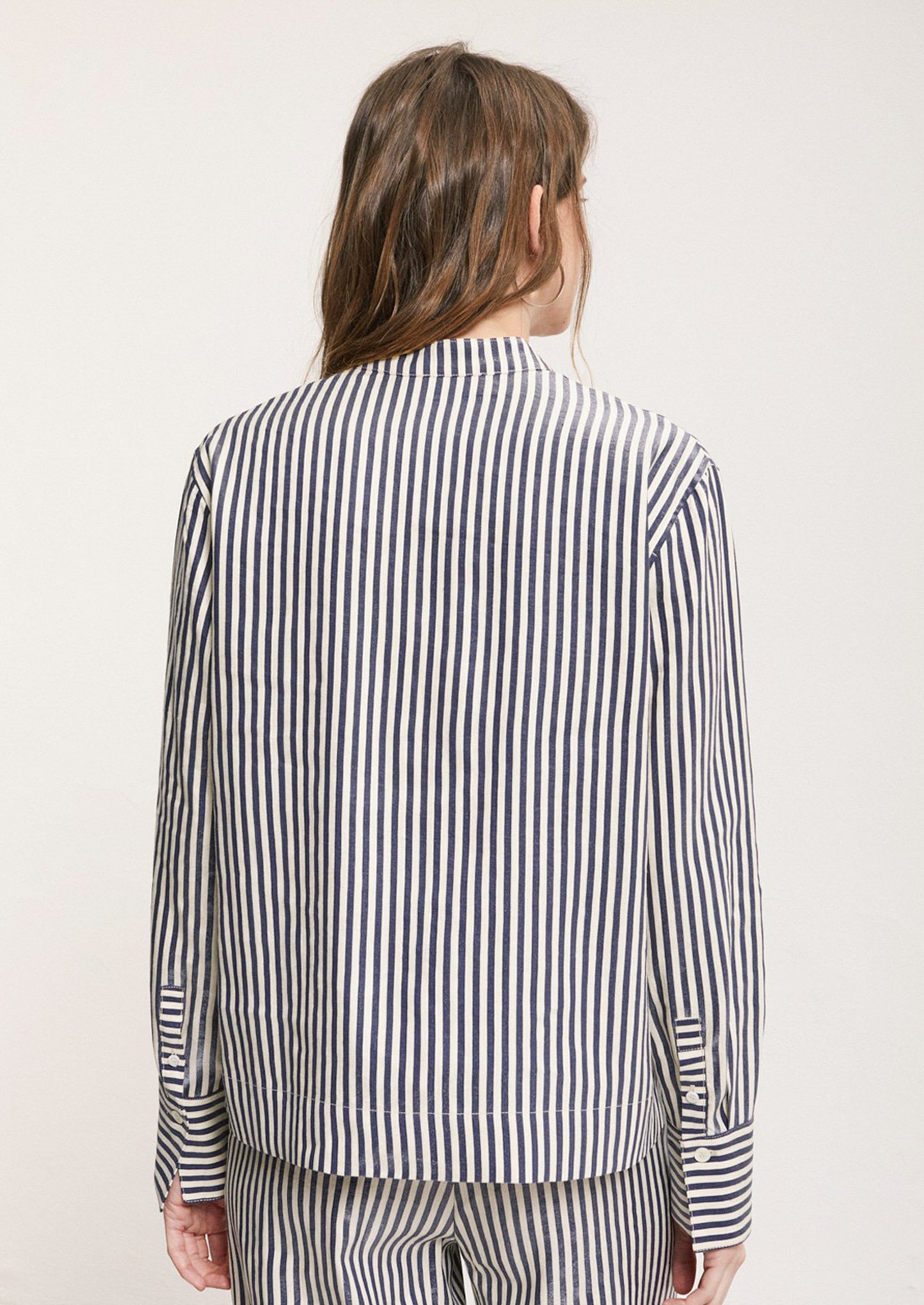 A woman wearing a striped long sleeve shirt in metallic navy blue and cream stripe.
