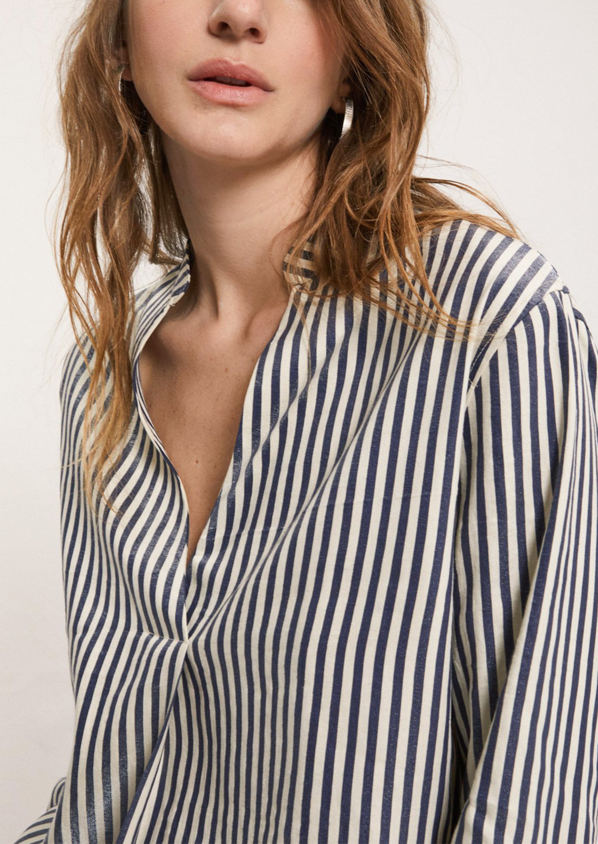 A woman wearing a striped long sleeve shirt in metallic navy blue and cream stripe.