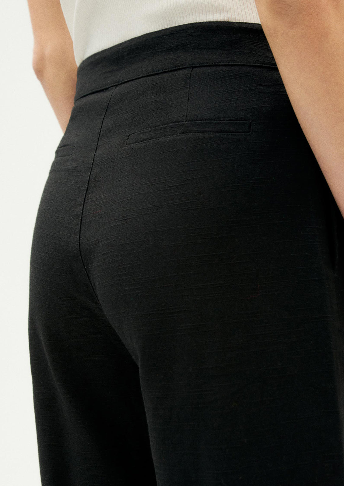 A person wearing a pair of ankle length cotton pants in black with slight wide leg.