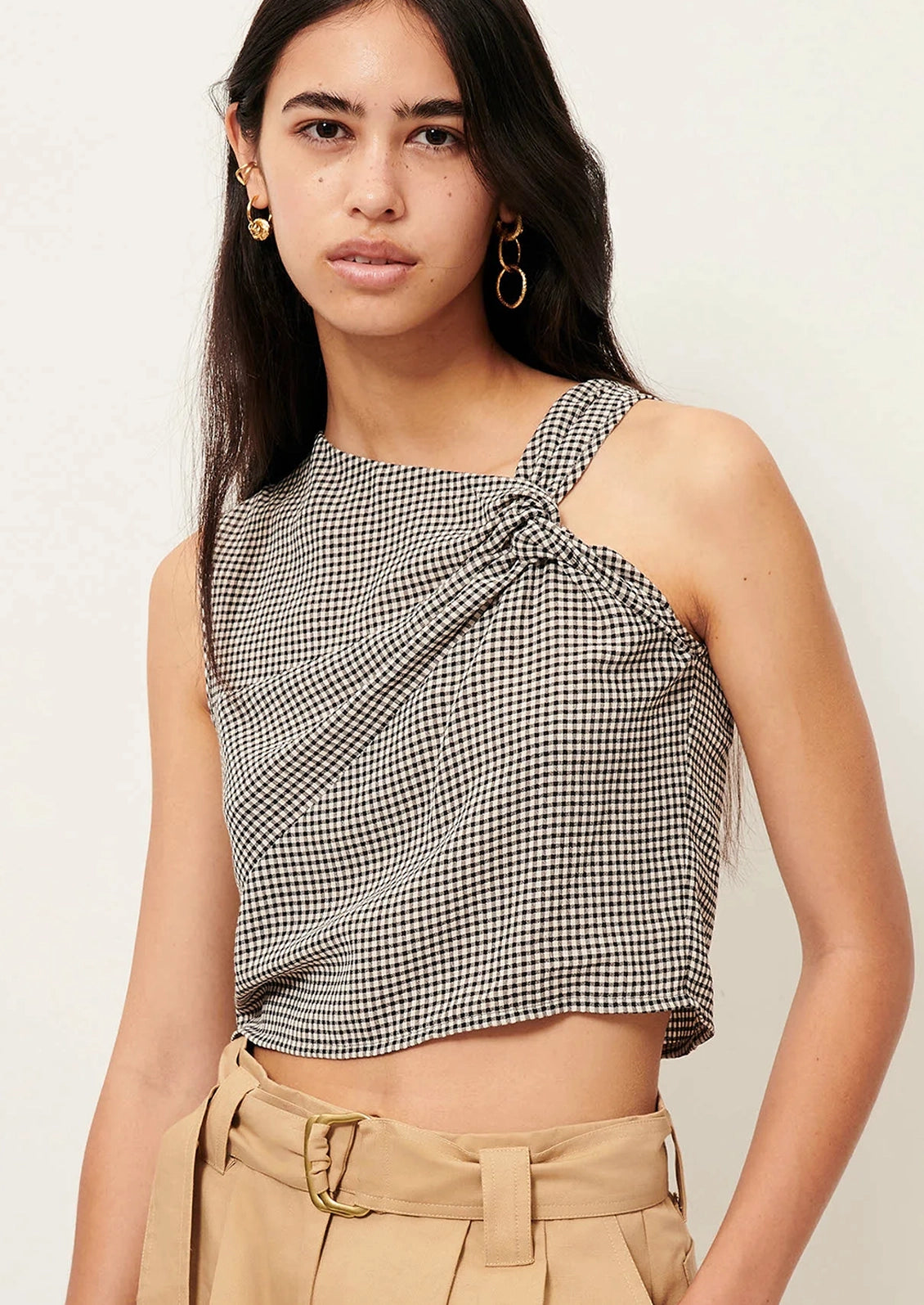 Woman wearing a black and white checkered top with beige pants on a light background