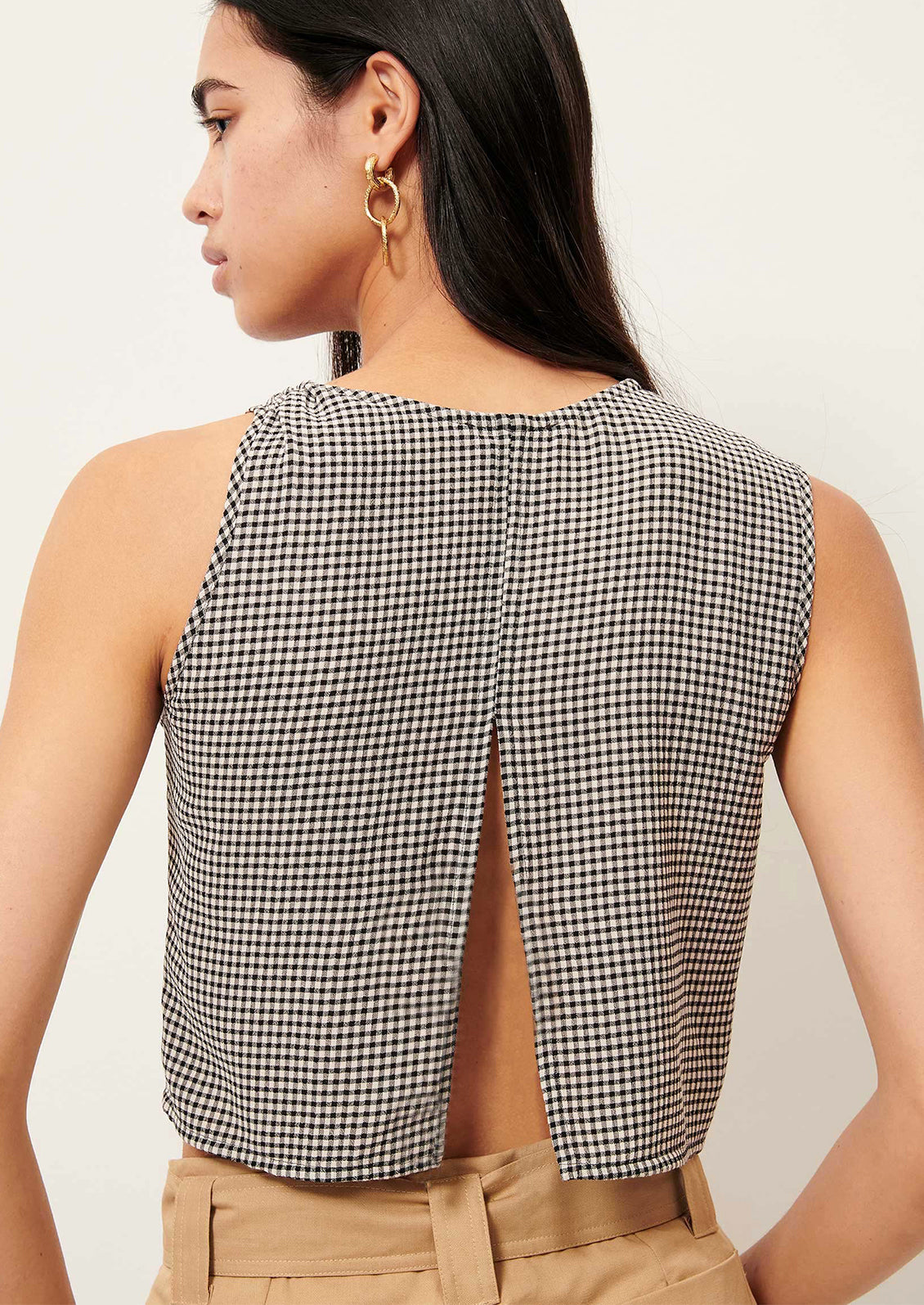 Woman wearing a black and white checkered sleeveless top with a cutout back on a plain background