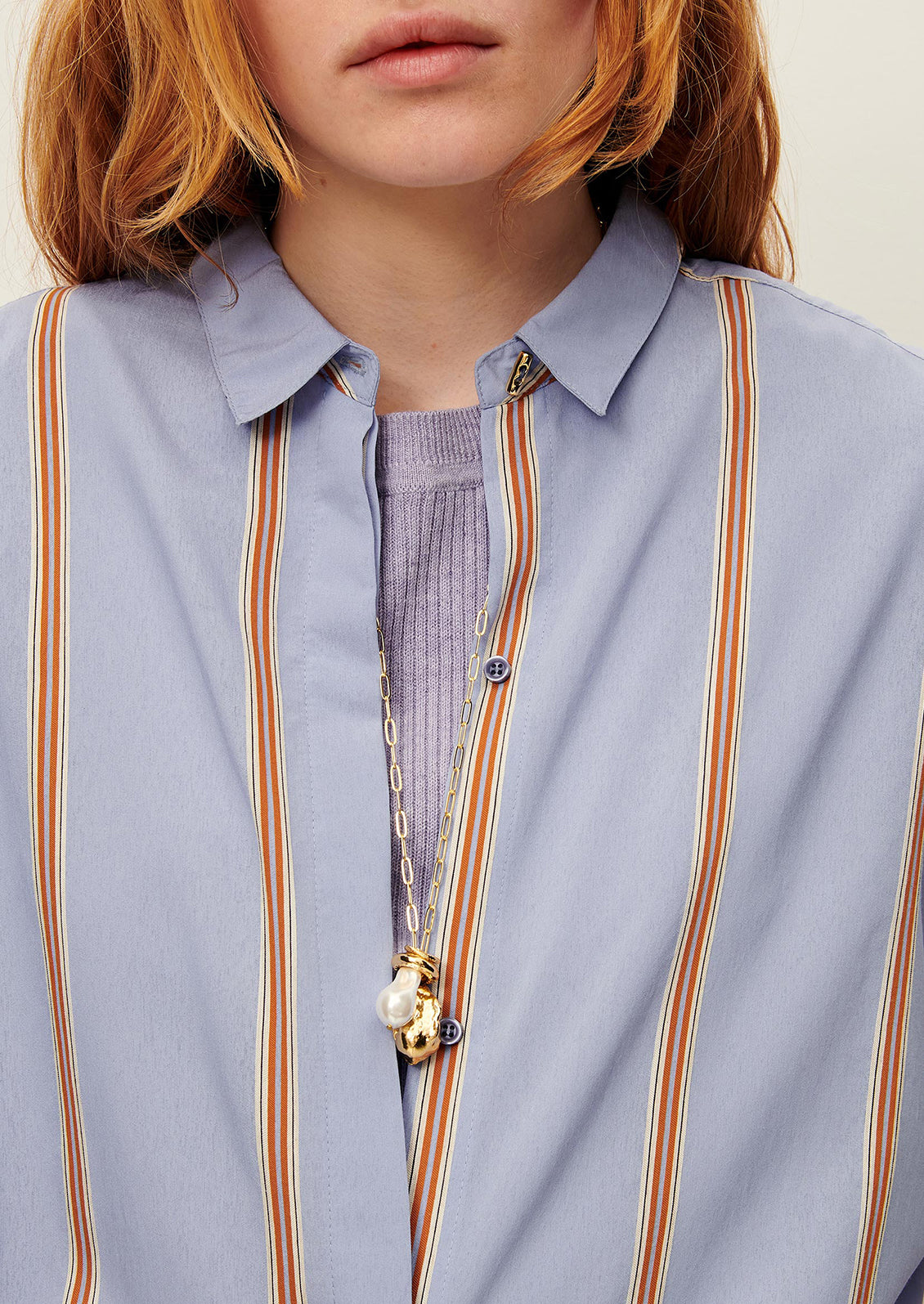 A person wearing a relaxed button front shirt in periwinkle with auburn stripes.