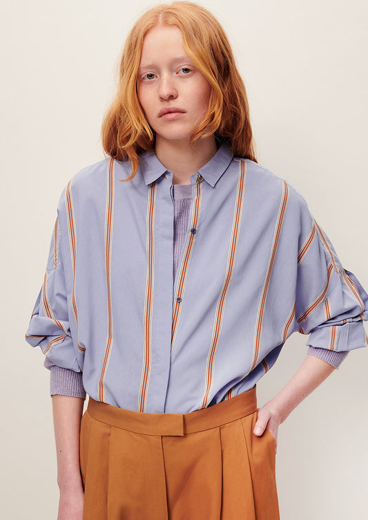 A person wearing a relaxed button front shirt in periwinkle with auburn stripes.
