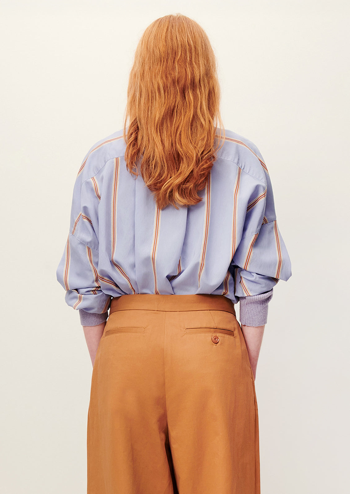 A person wearing a relaxed button front shirt in periwinkle with auburn stripes.