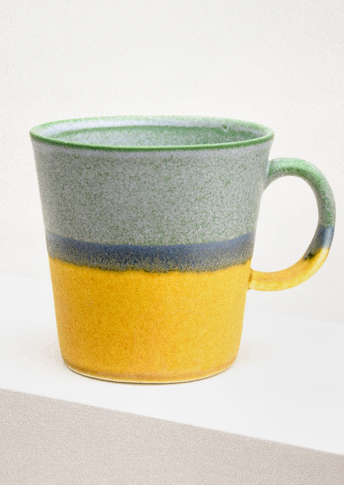Ceramic mug with green top and yellow bottom on a light background