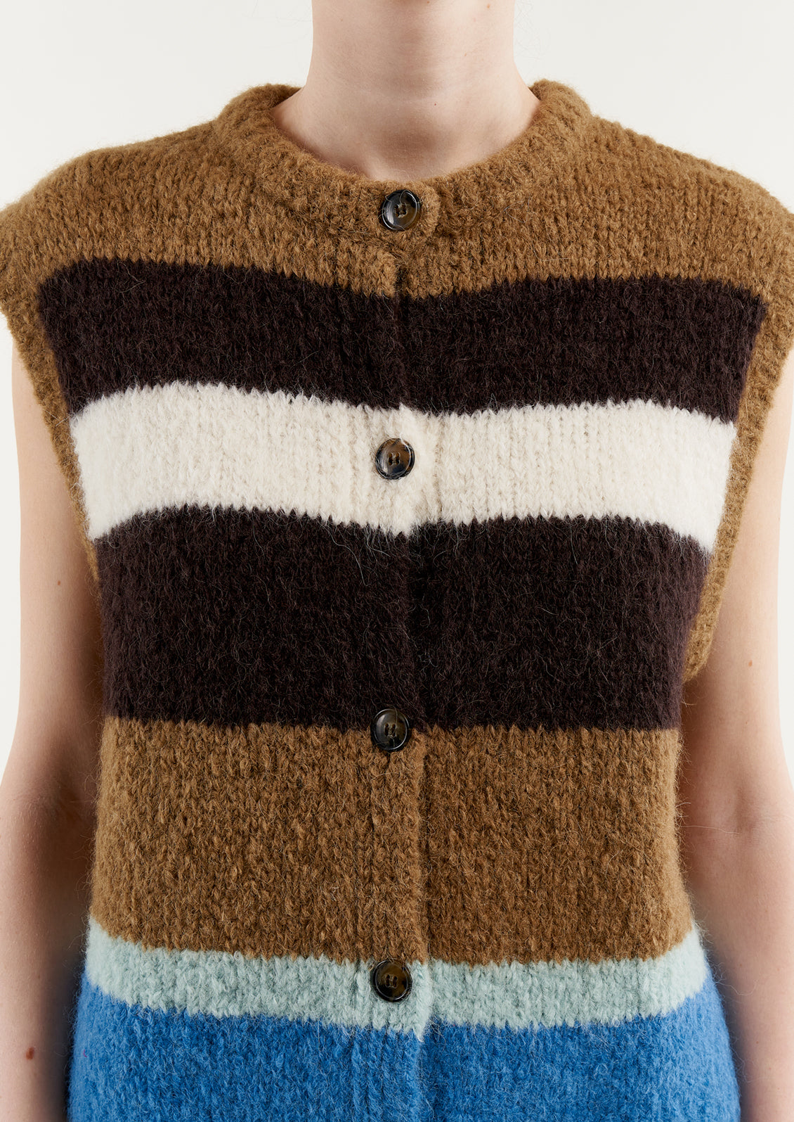 A woman wearing a sleeveless, button front sweater vest in brown and blue stripes.