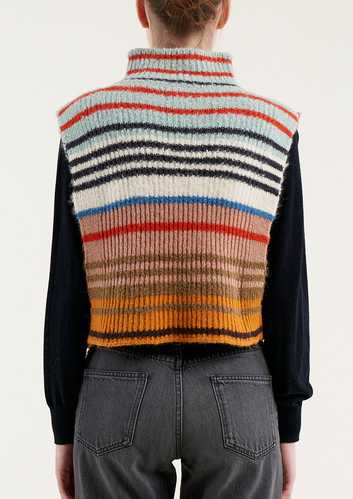 A person wearing a sleeveless turtleneck sweater in multicolor stripe.
