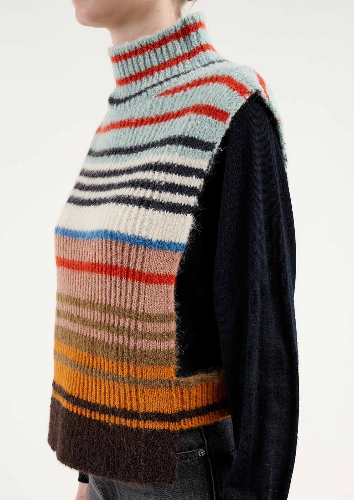 A person wearing a sleeveless turtleneck sweater in multicolor stripe.