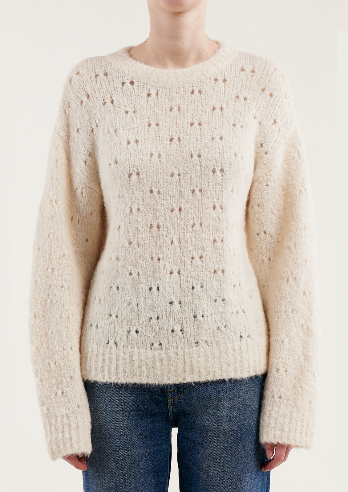 A woman wearing a fuzzy cream colored sweater with double birdseye cutout pattern throughout.