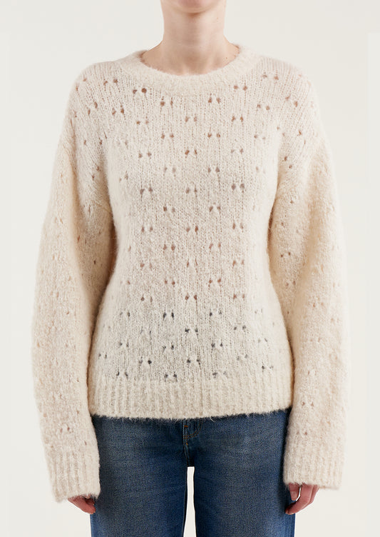 A woman wearing a fuzzy cream colored sweater with double birdseye cutout pattern throughout.