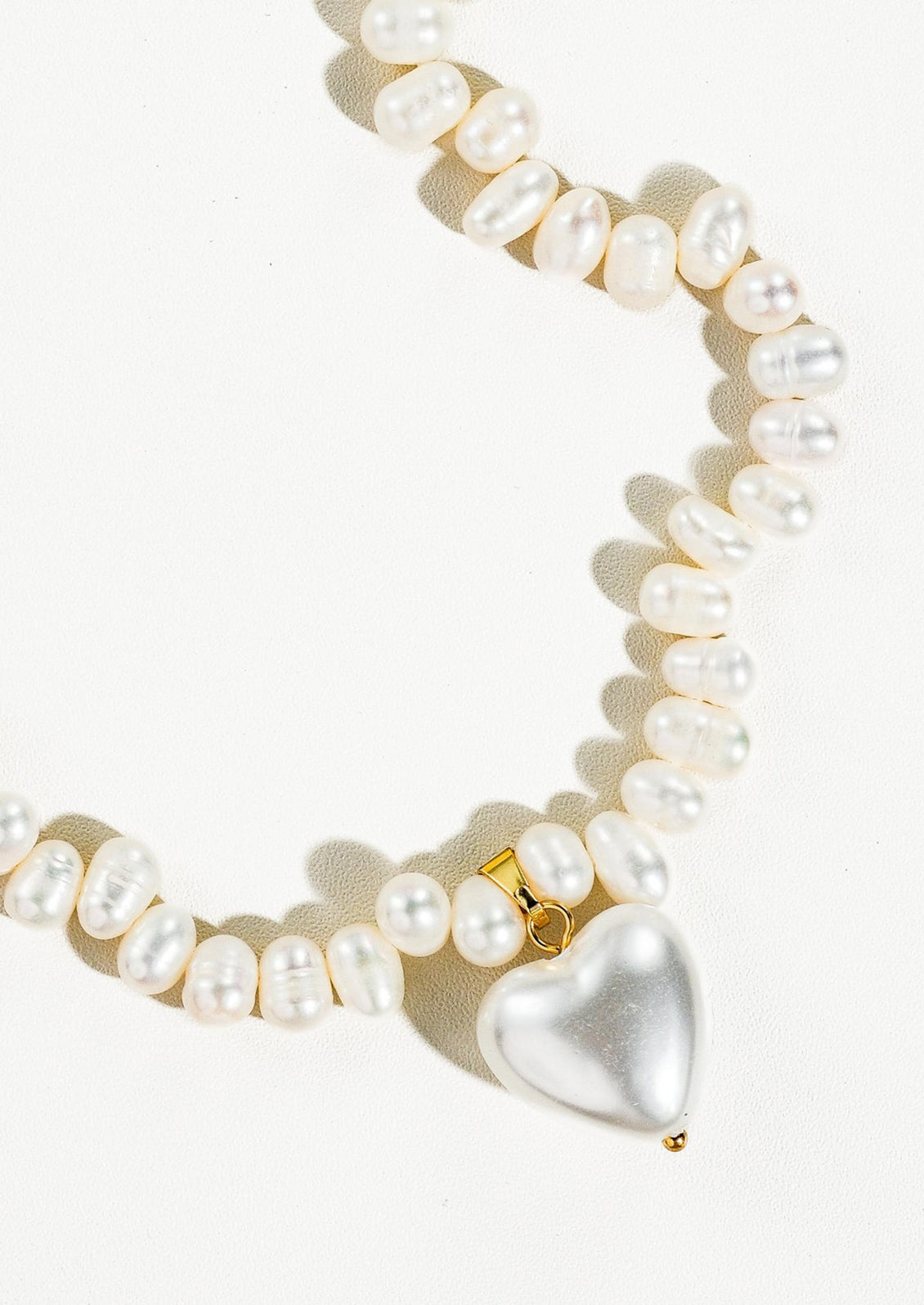 A white baroque pearl necklace with white pearlized heart shaped charm.