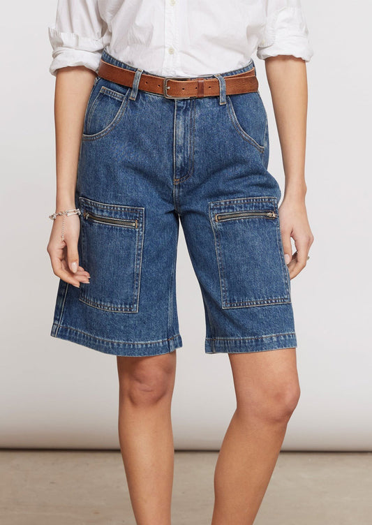 A person wearing a pair of knee-length denim shorts with zip details on patch pockets.