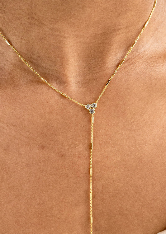 A close-up of a gold Y-necklace with a small three-stone floral cluster at the center, worn on a model's neck.