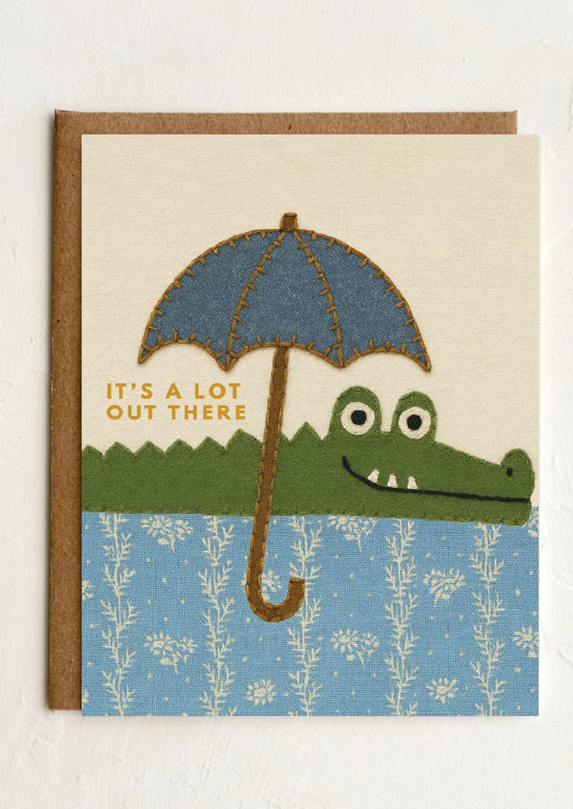 Card with an illustration of a crocodile holding an umbrella and text 'It's a lot out there' on a white background.