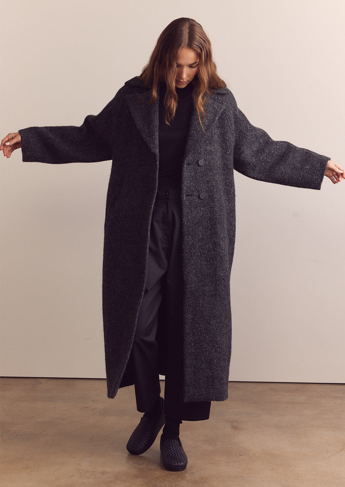 A woman wearing a long wool coat in dark grey speckled wool.