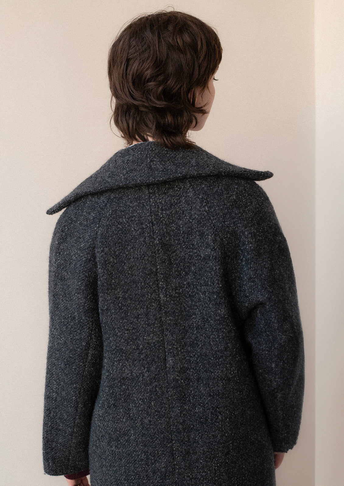 A woman wearing a long wool coat in dark grey speckled wool.